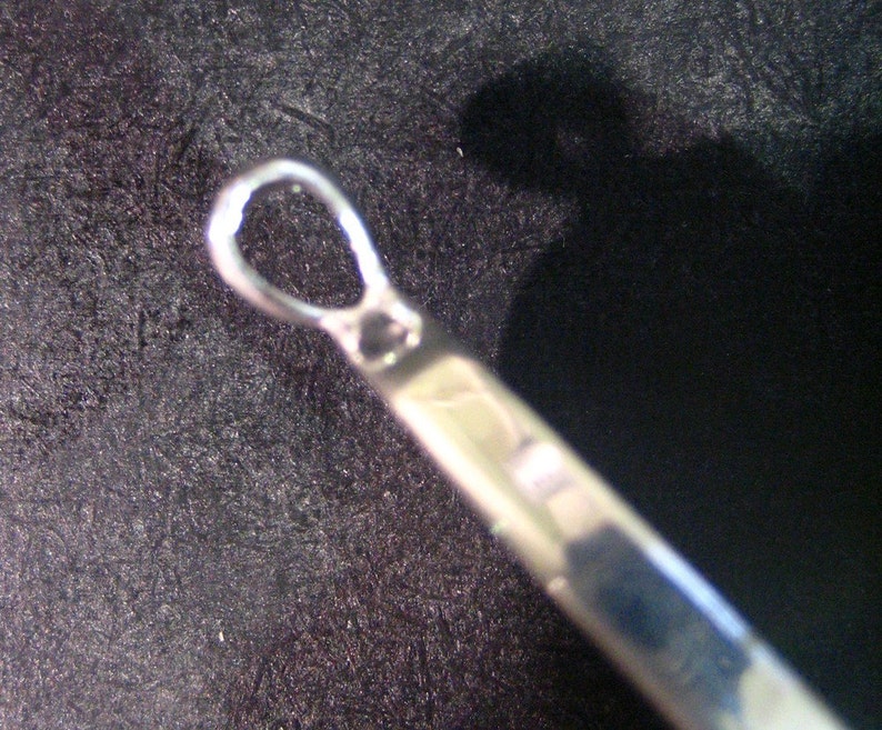 May include: Close-up of a silver metal loop with a smooth, rounded surface. The loop is part of a larger object, possibly a piece of jewelry or a decorative element.