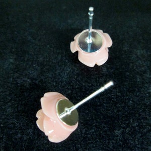 May include: A pair of pink rose stud earrings with silver posts. The earrings are made of a smooth, shiny material.