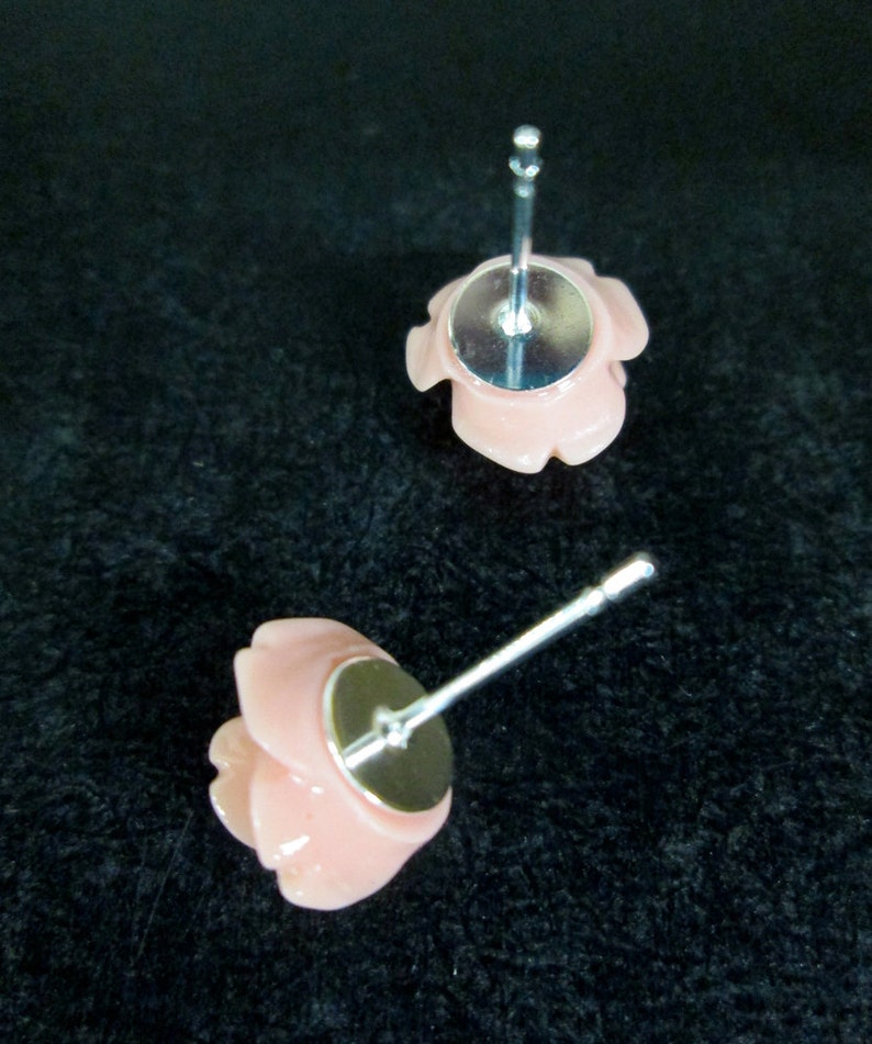 May include: A pair of pink rose stud earrings with silver posts. The earrings are made of a smooth, shiny material.