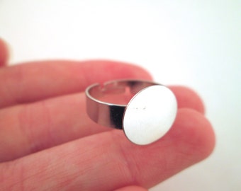 May include: A silver ring with a round, blank, silver-toned bezel. The bezel is approximately 2.5 cm in diameter.