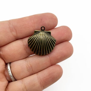 May include: A gold-toned metal seashell charm with a detailed, ribbed texture. The charm has a loop at the top for attaching to jewelry or other crafts.
