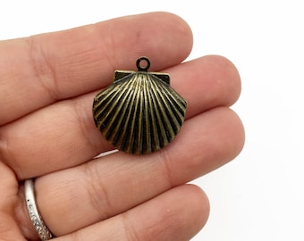 May include: A gold-toned metal seashell charm with a detailed, ribbed texture. The charm has a loop at the top for attaching to jewelry or other crafts.