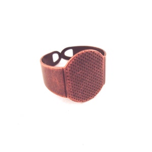 May include: A copper-toned ring with a round, textured bezel. The ring is designed to hold a small, round cabochon.