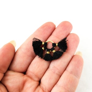 以下が含まれることがあります： 3つの黒いタッセルチャームが付いたゴールドのフープイヤリング