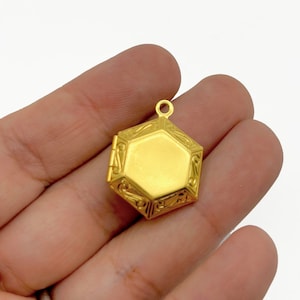May include: Gold-toned hexagonal locket pendant with an ornate design. The locket has a hinged opening and a loop for attaching a chain.