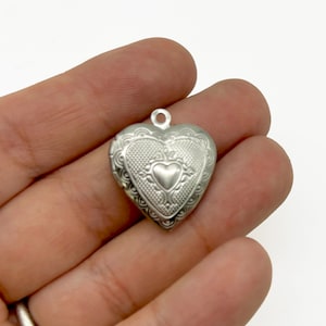 Könnte beinhalten: Silbernes herzförmiges Medaillon mit einem filigranen Design und einem kleineren Herzen in der Mitte.