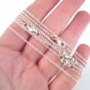 May include: A set of five silver chain necklaces of varying lengths, displayed on a hand.