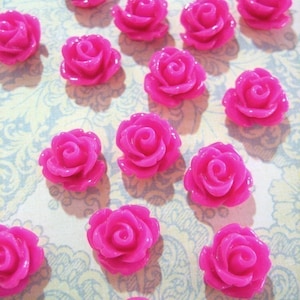 May include: A collection of 14 bright pink plastic rose embellishments. The roses are all the same size and shape, and they have a glossy finish.