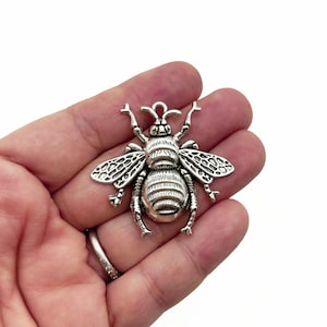 Op de afbeelding: Zilverkleurige bij-bedel met gedetailleerde vleugels en lichaam. De bedel heeft een lus aan de bovenkant om aan sieraden of andere knutselwerkjes te bevestigen.