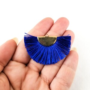 May include: A blue tassel fringe trim with a gold metal half-circle accent. The tassel fringe is a popular embellishment for clothing, accessories, and home decor.