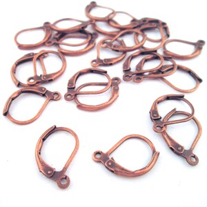 May include: A group of 18 copper-toned earring hooks, also known as leverback earring findings, are scattered on a white surface. The hooks are made of metal and have a smooth, polished finish.