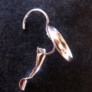 May include: Silver clip-on earring with a smooth, rounded design. The earring has a curved hook and a secure clasp.