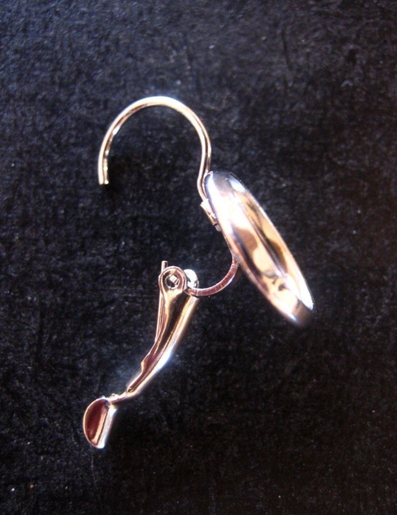 May include: Silver clip-on earring with a smooth, rounded design. The earring has a curved hook and a secure clasp.