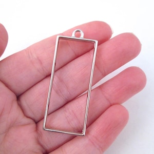 Peut inclure: Pendentif en métal argenté avec un cadre rectangulaire. Le cadre est ouvert sur tous les côtés et a une boucle en haut pour accrocher.