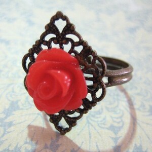 May include: A red rose ring with a filigree design. The ring is made of metal and has a delicate, intricate design.