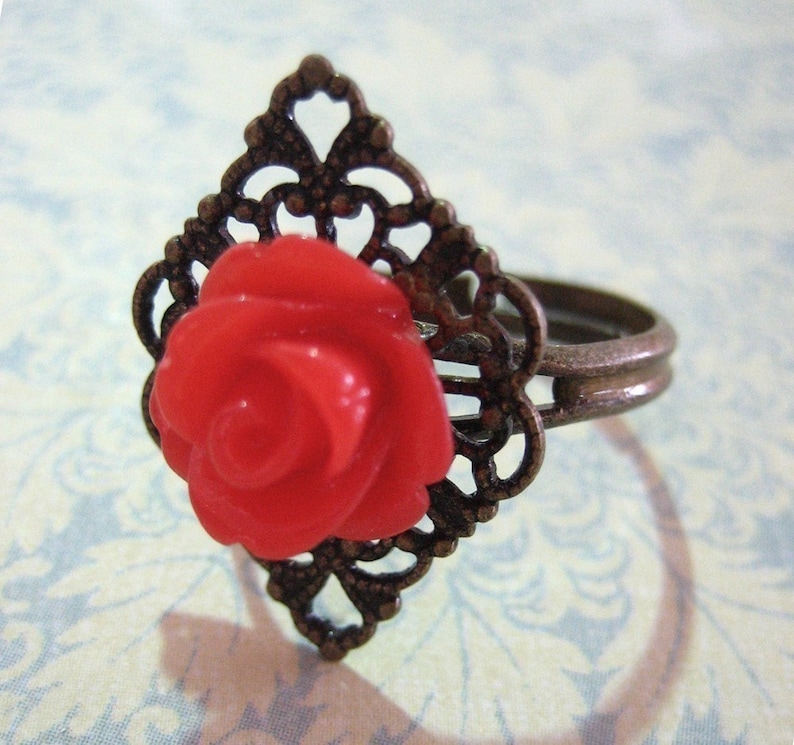 May include: A red rose ring with a filigree design. The ring is made of metal and has a delicate, intricate design.