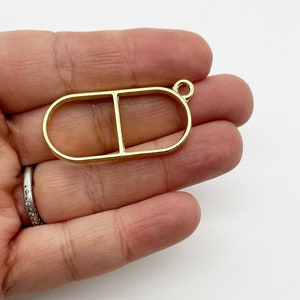 Peut inclure: Pendentif en métal doré en forme de capsule avec une capsule plus petite à l'intérieur. Le pendentif a une boucle en haut pour attacher une chaîne.