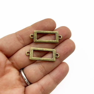May include: Two antique gold-toned metal rectangular frame connectors with two jump rings on each side.