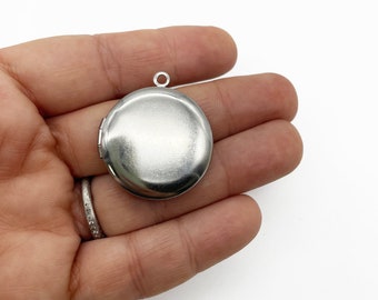 May include: A silver locket pendant with a round, smooth surface. The locket has a hinged lid and a loop for attaching a chain.