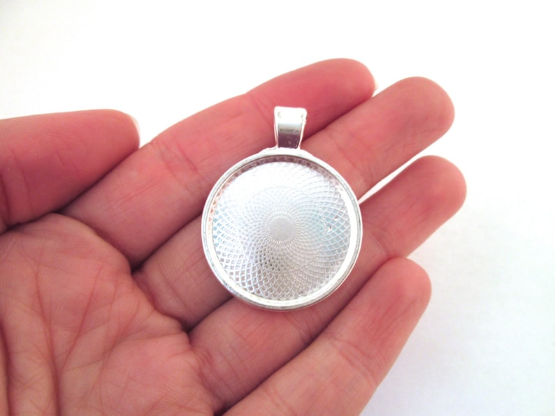 May include: Silver pendant with a round, clear glass bezel. The bezel has a textured, circular pattern.