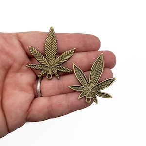 May include: Two antique gold-toned metal cannabis leaf charms with a loop for hanging.