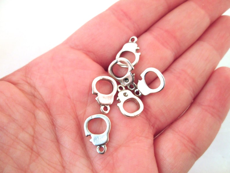 Pode incluir: Seis pingentes de metal prateados em forma de algemas. Os pingentes s&atilde;o pequenos e delicados, perfeitos para adicionar um toque de fantasia a joias ou artesanato.