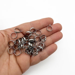 May include: A pile of silver metal jump rings with a small loop on one side. The rings are about 1/2 inch in diameter.