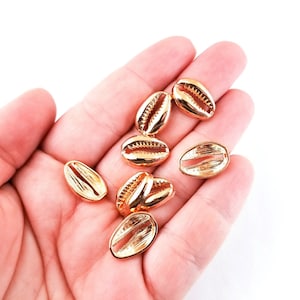 May include: A collection of gold-colored cowrie shells, a type of seashell, in a hand. The shells are smooth and shiny.
