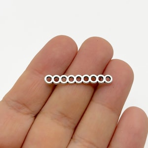 May include: Silver metal connector with a row of ten open circles. The connector is about 1 inch long.