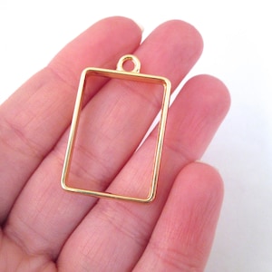 May include: Gold-toned metal pendant frame with a rectangular shape and a loop at the top for hanging.