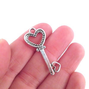 Puede incluir: Encanto de llave de corazón plateado con un borde de cuentas. La llave tiene un pequeño lazo en forma de corazón en la parte inferior.