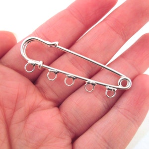 May include: Silver-toned safety pin with five jump rings attached. The pin is open and ready to be used.