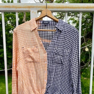 May include: A long-sleeved button-down shirt with a gingham pattern. The left side of the shirt is orange and white, while the right side is black and white. The shirt is tied at the waist.
