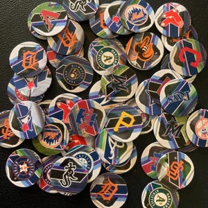 May include: A collection of colorful round baseball team logo tokens. The tokens feature logos for teams such as the Astros, Athletics, Brewers, and Nationals.