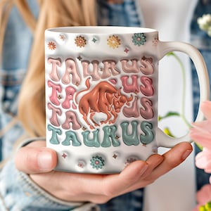 May include: White ceramic mug with a colourful retro design featuring the word "Taurus" repeated multiple times and a brown bull illustration in the centre.