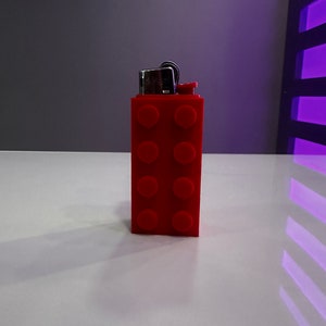 Peut inclure: Un briquet en plastique rouge en forme de brique Lego.