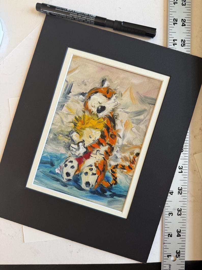 May include: An oil painting of Calvin and Hobbes hugging, set in a white frame on a black mat. The artwork features vibrant colors and brushstrokes, depicting the iconic characters in a tender embrace. A black pen and ruler are in the background.
