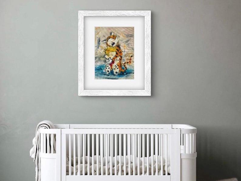 May include: A framed print featuring a watercolor illustration of a boy and a tiger hugging. The artwork is in a white frame and hangs above a white crib. The illustration has a blue, orange, and white color scheme.