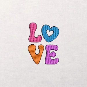May include: Embroidered design spelling "LOVE" in colorful, textured letters. The "L" is pink, the "O" is a blue heart, the "V" is orange, and the "E" is purple. The design is on a white fabric background.