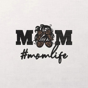 May include: Embroidered design on a white background. The design features the word "MOM" in bold black letters, with a stylized image of a woman's hair, bow, and sunglasses in the center. Below, the text reads "#momlife" in a cursive font.