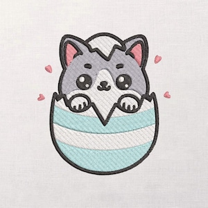 Puede incluir: Diseño bordado de un lindo gato de dibujos animados saliendo de un huevo agrietado. El gato tiene pelaje gris, orejas rosas y ojos grandes y redondos. El huevo es de rayas azules y blancas. Corazones rosas flotan alrededor del gato.