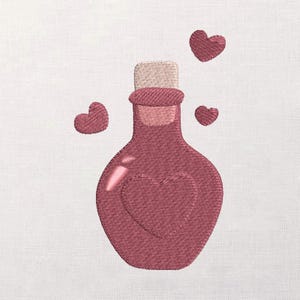 Puede incluir: Diseño bordado de una botella de poción granate con forma de corazón en la parte delantera y un tapón de corcho. Tres corazones granates flotan alrededor de la botella. El diseño está sobre un fondo blanco.