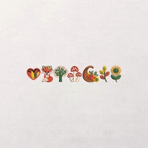 May include: Embroidered autumn-themed designs on white fabric. The designs include a heart, fox, tree, mushrooms, cornucopia, leaves, and a sunflower. The colours are primarily red, orange, yellow, green, and brown.