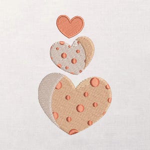 May include: Embroidered design of three hearts stacked vertically. The top heart is solid peach, while the two lower hearts are peach with peach polka dots. The hearts are on a white background.