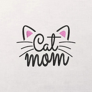 May include: Embroidered design featuring the words "Cat mom" in a cursive font, with cat ears and whiskers. The ears are outlined in black with pink inner ears. The design is on a white background.