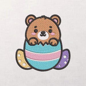 May include: An embroidered design of a brown bear emerging from a cracked Easter egg. The egg is decorated with blue, pink, yellow, and purple sections. The bear has a black outline, pink cheeks, and a small black nose.