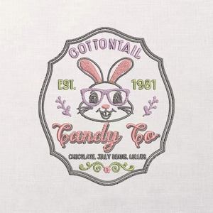 以下が含まれることがあります： メガネをかけたウサギの刺繍パッチ。テキストは「Cottontail Candy Co.」と「Est. 1981」です。デザインにはピンク、紫、緑、グレーの色が含まれており、下部には「Chocolate, Jelly Beans, Lollipops」という言葉があります。