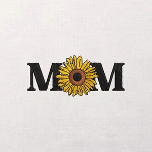 May include: Embroidered design featuring the word "MOM" in black capital letters, with a yellow sunflower replacing the "O". The sunflower has a brown center and yellow petals. The design is on a white background.
