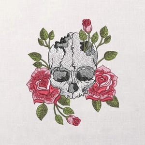 Pode incluir: Design bordado de uma caveira detalhada com rachaduras e sombreamento, rodeada por rosas vermelhas vibrantes e folhas verdes. A caveira tem órbitas escuras e uma textura detalhada, criando um tema floral gótico.