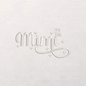 May include: Embroidered design on a white fabric. The word "Mimi" is written in a cursive font, with a butterfly and star accents. The embroidery is in a light silver color.
